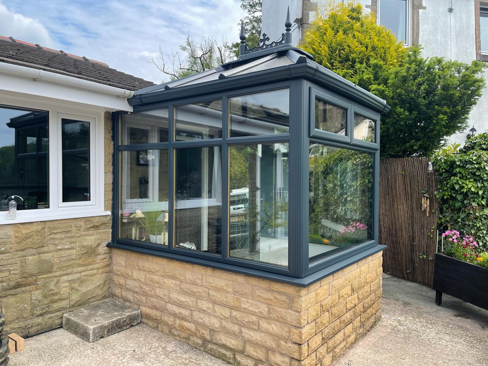 A conservatory with its frames sprayed anthracite, stone base and pitched glass roof