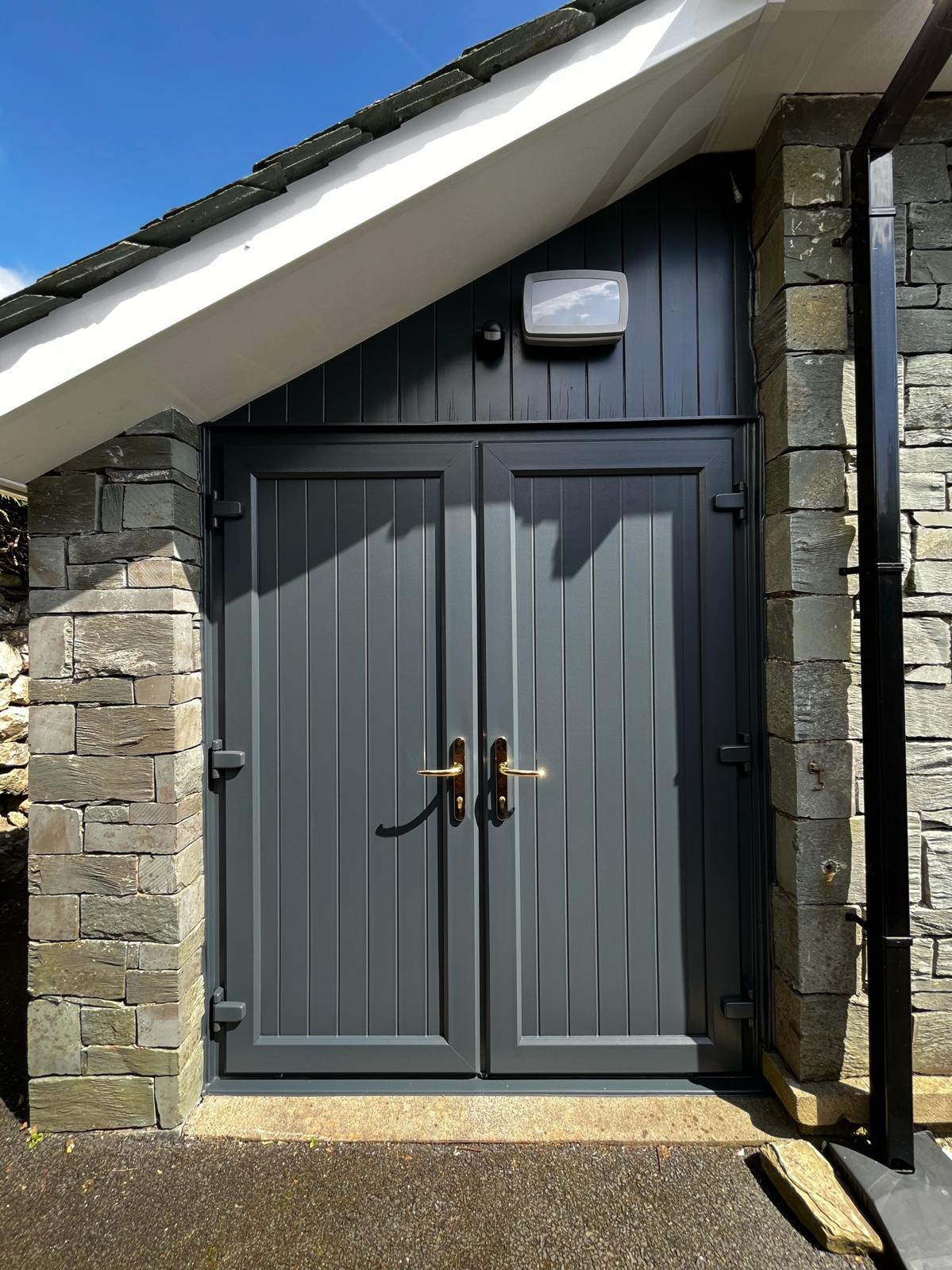 Double garage doors sprayed grey under a stone gable