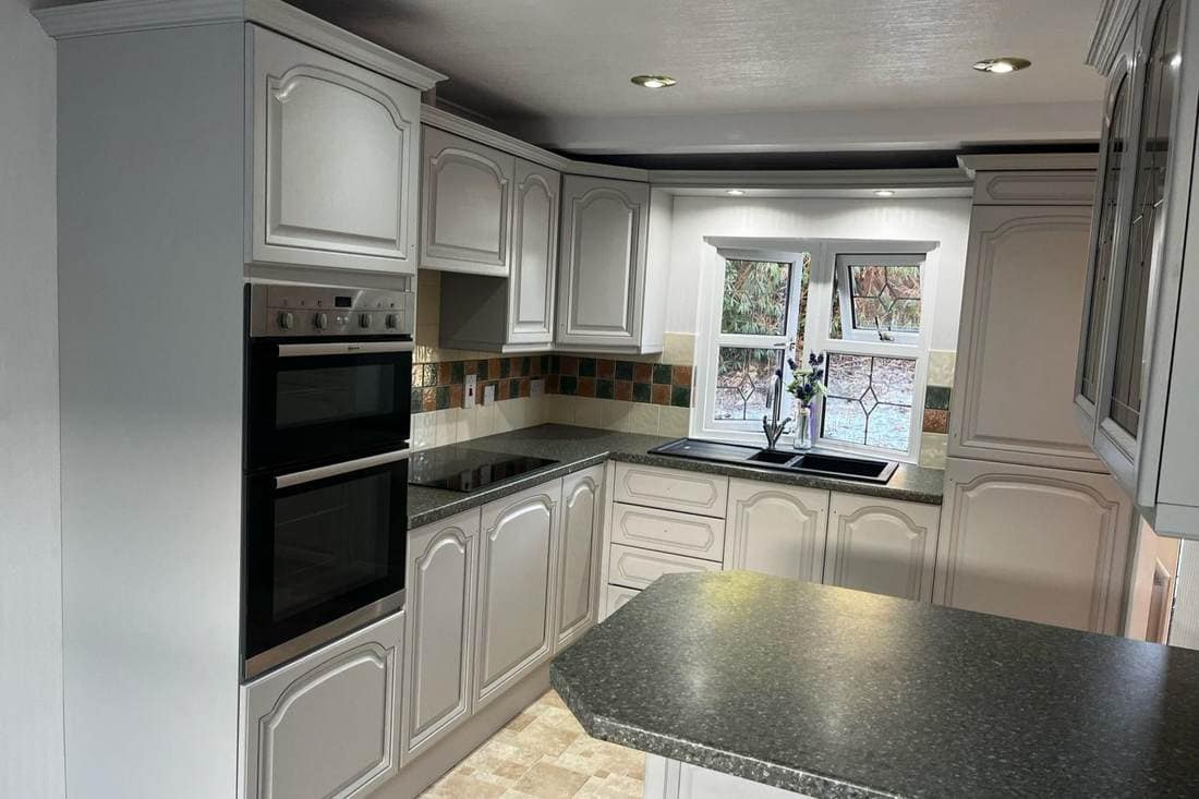 The same traditional kitchen after respraying, with the oak doors in cream beneath a dark worktop