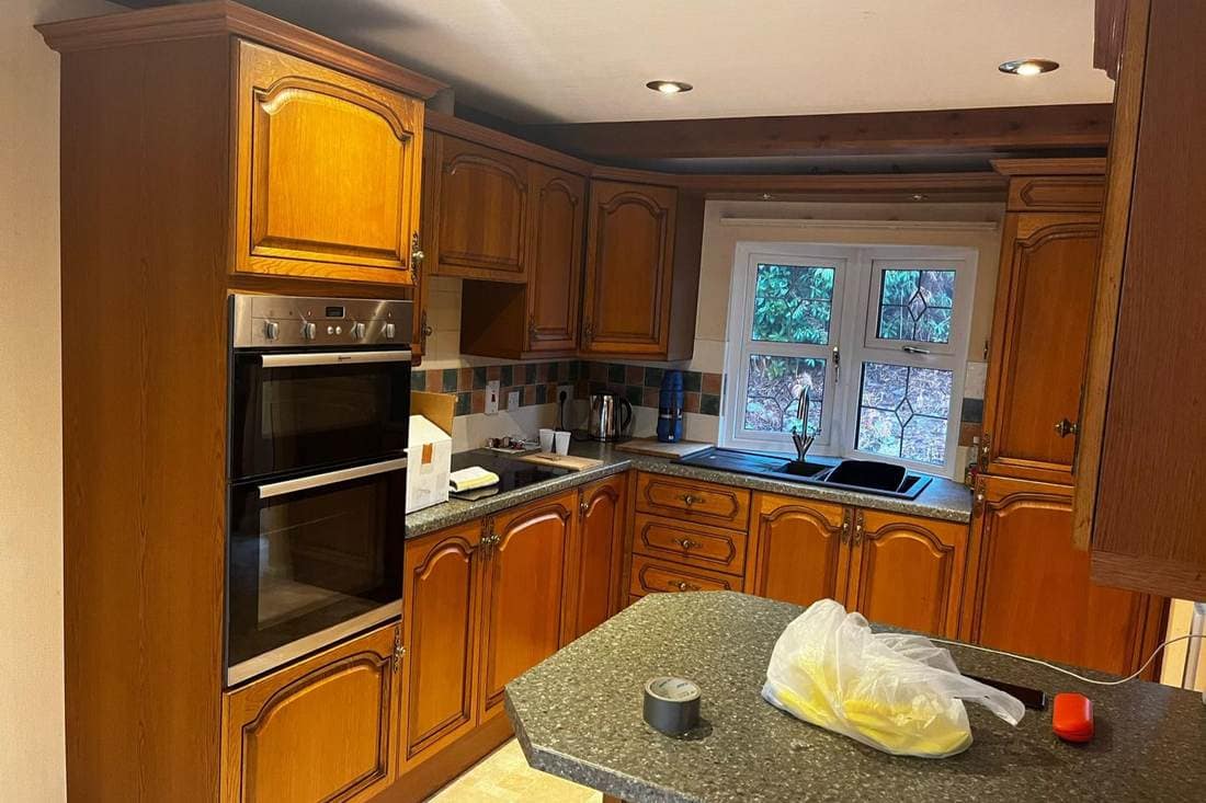 Traditional kitchen before respraying, with orange-toned oak doors and a mottled green worktop