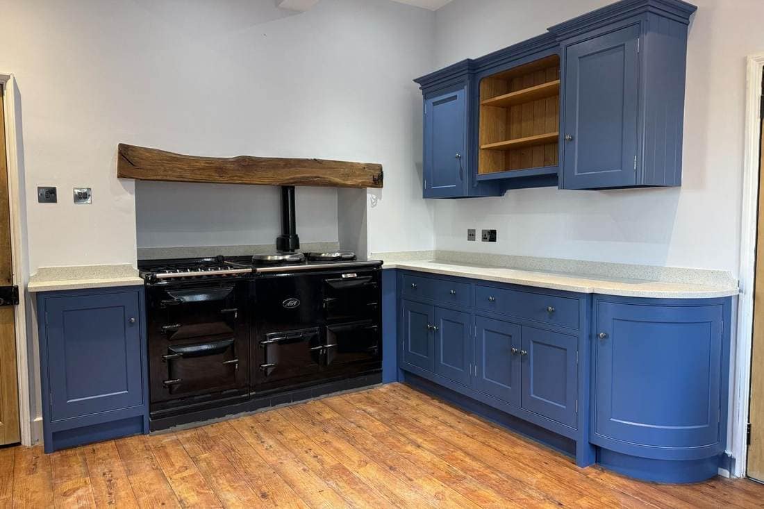 Kitchen before respraying, with deep blue units either side of a black Aga under a reclaimed oak mantel