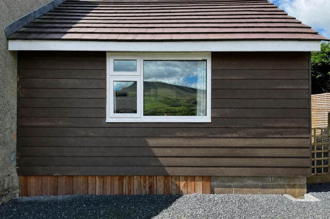 Garden room before spraying, with dark brown stained cladding and a white uPVC window