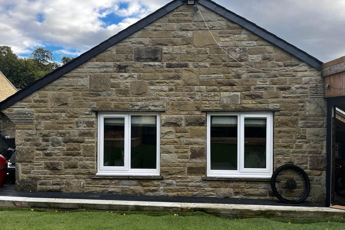 Stone gable end before spraying, with two white uPVC windows