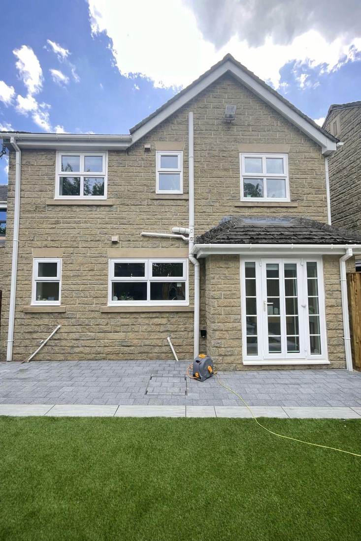 Rear of a new stone-built house before spraying, with white uPVC windows and white french doors