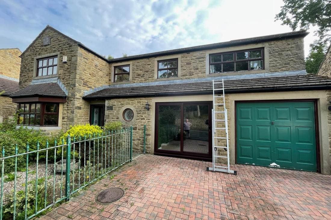 Rear of a stone house before spraying, with a green garage door, dark brown window frames and green railings