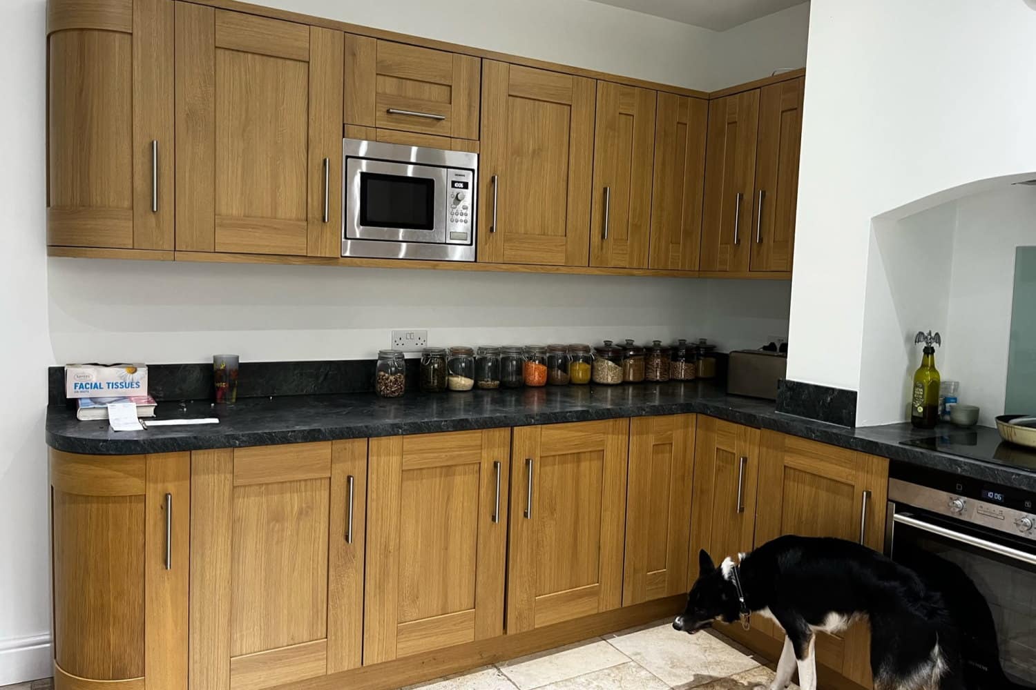 A shaker kitchen before respraying, with orange-toned oak doors, curved end units and a dark speckled worktop