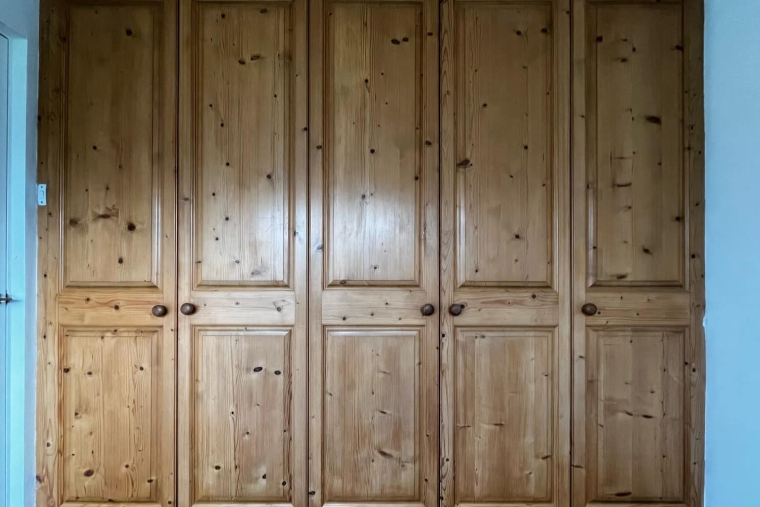 A five-door run of fitted pine wardrobes before spraying, with knotted grain and wooden knobs
