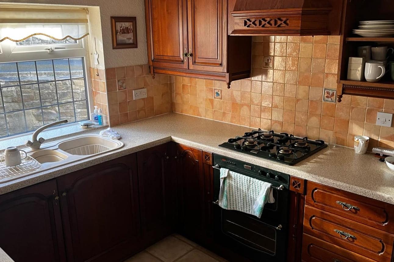 A dated kitchen before respraying, with dark mahogany raised-panel doors and a carved extractor canopy