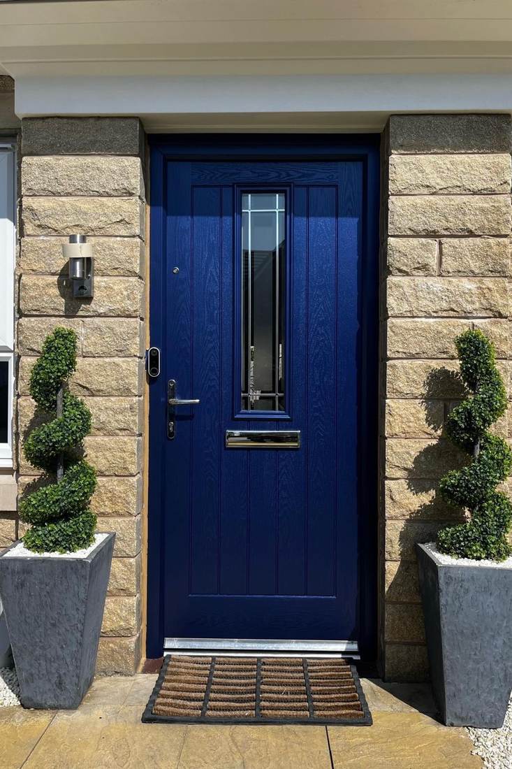 A deep blue composite front door in a stone surround, flanked by topiary in tapered planters