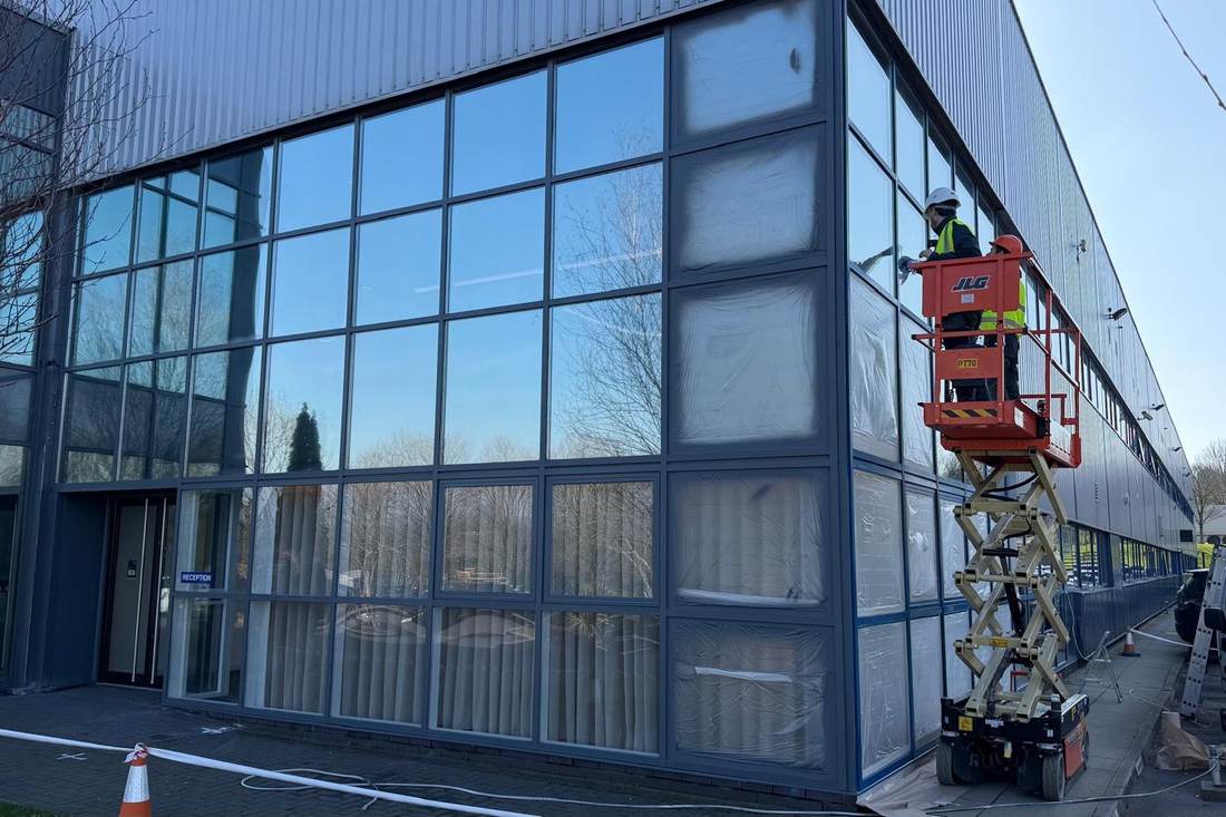 Spraying in progress on the commercial glazing, with the corner bays masked off and a scissor lift alongside