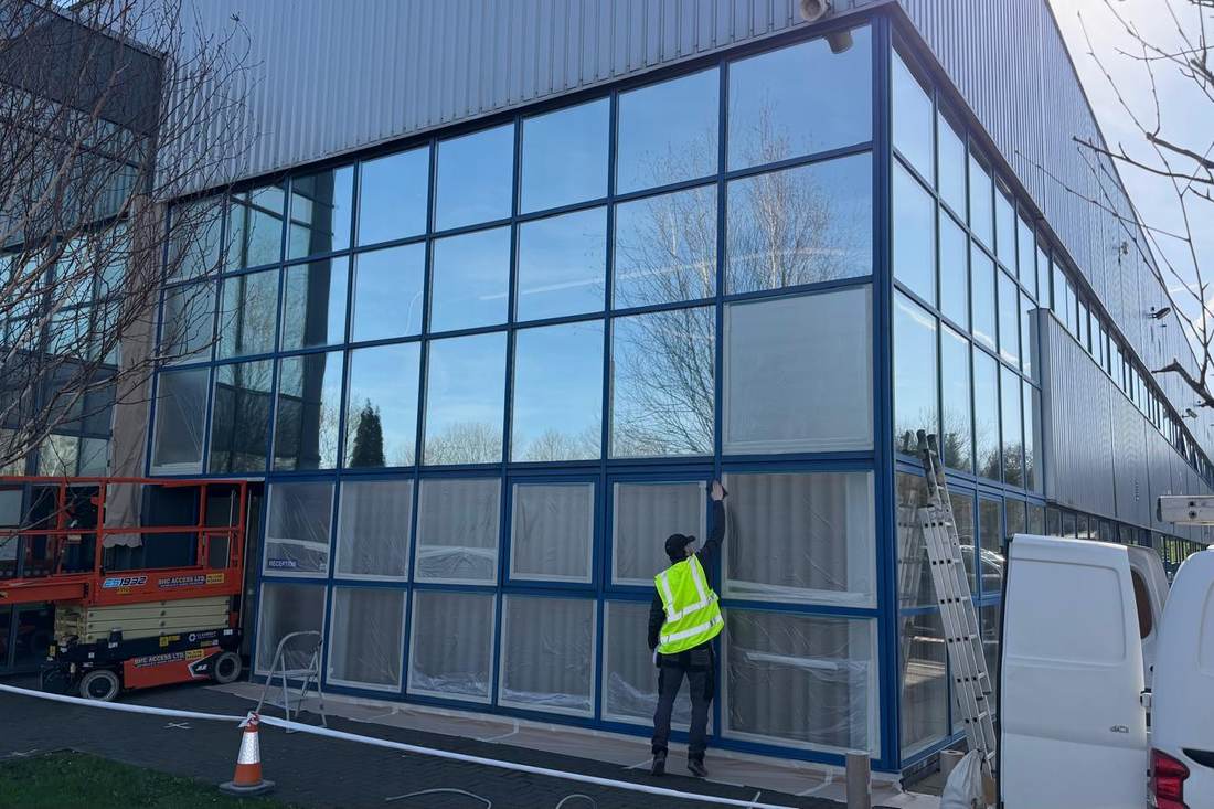 A sprayer in hi-vis working along a glazed commercial elevation from a lift