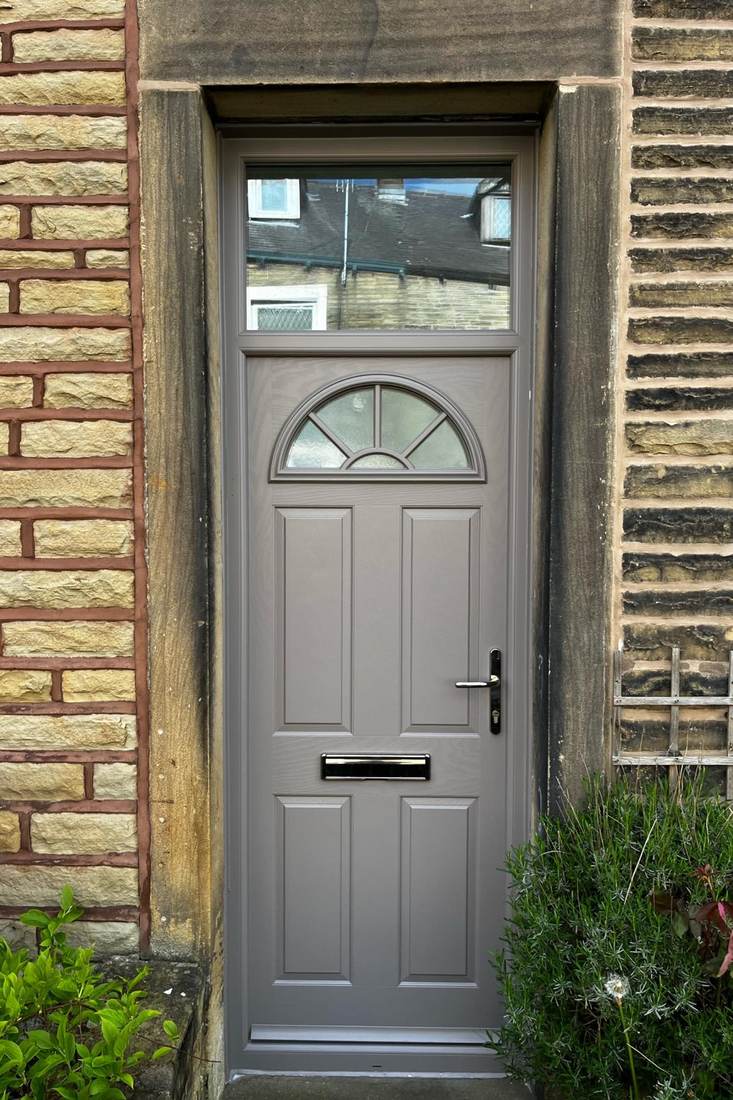 A grey composite front door with an arched fanlight in a stone doorway