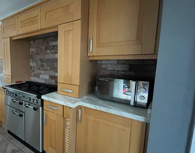 Galley kitchen before respraying, with light oak shaker doors, a brick splashback and a stainless range cooker