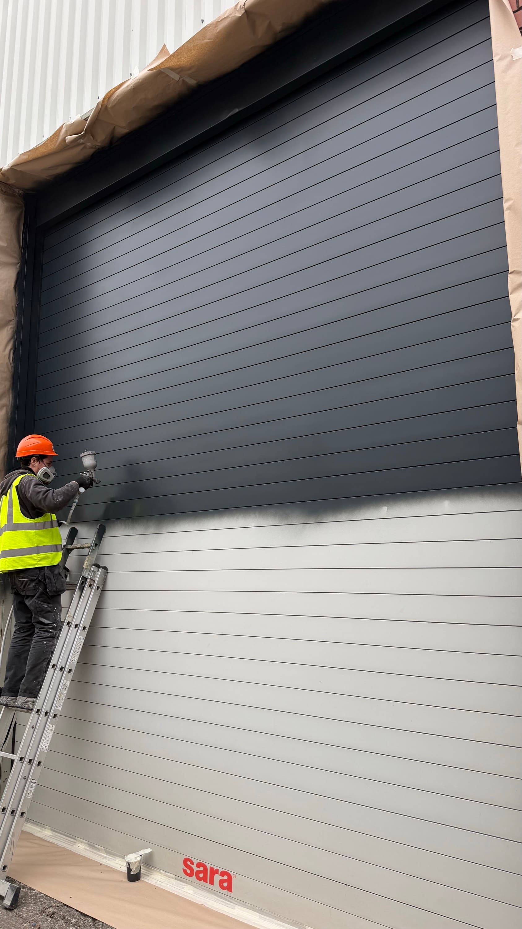 A roller shutter door being spray painted from grey to anthracite