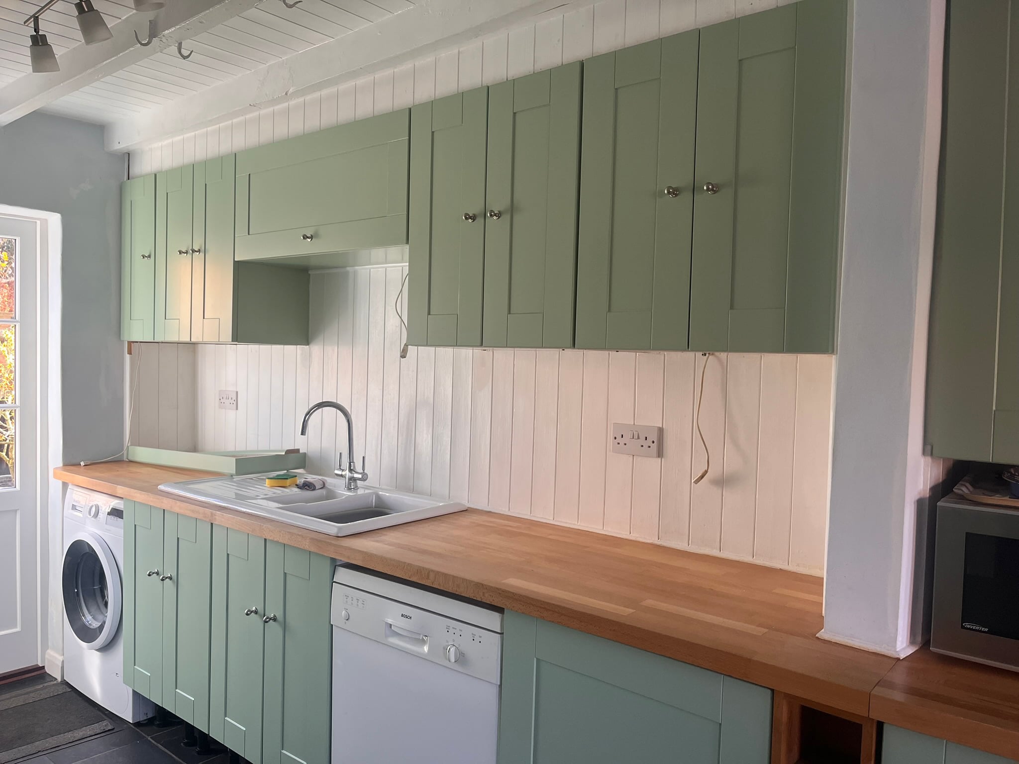 Green kitchen units and island after respraying, with brass handles