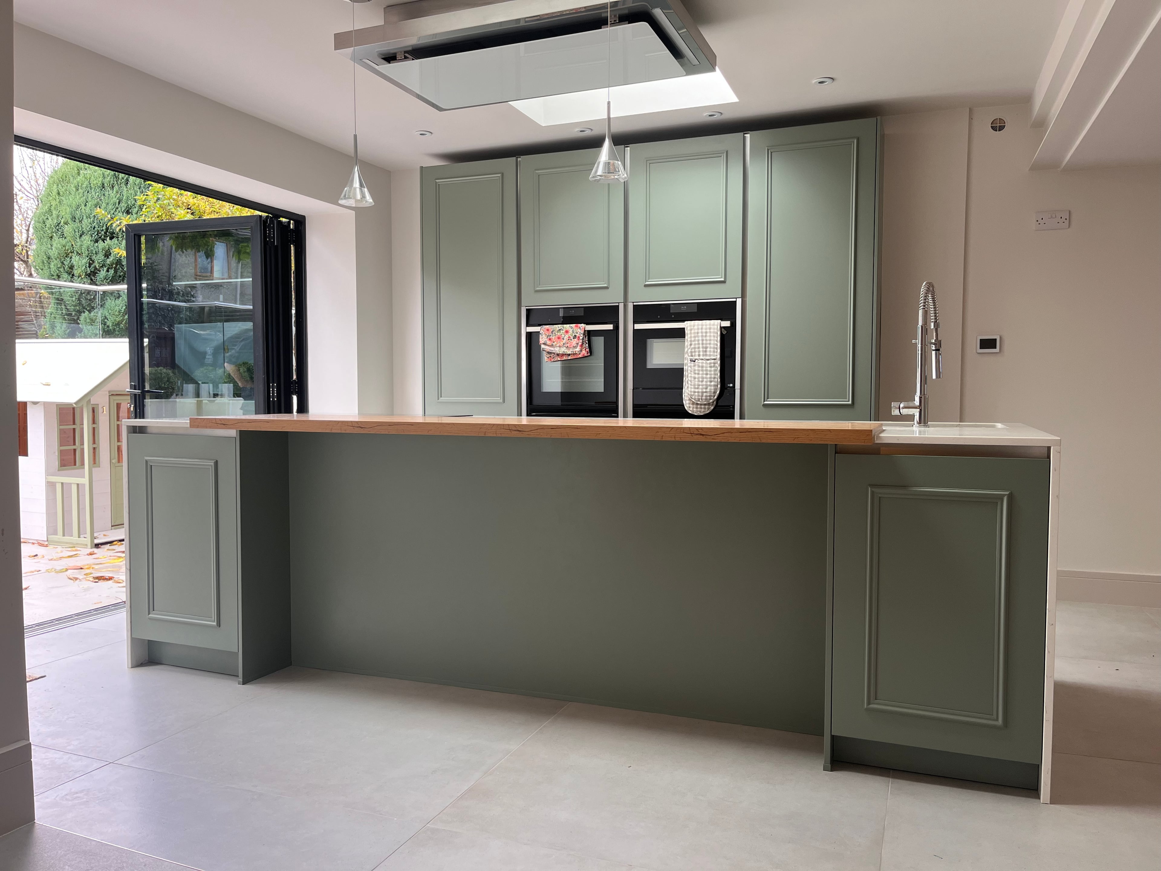 Sage green kitchen island with a wooden worktop, resprayed in a bright open-plan room